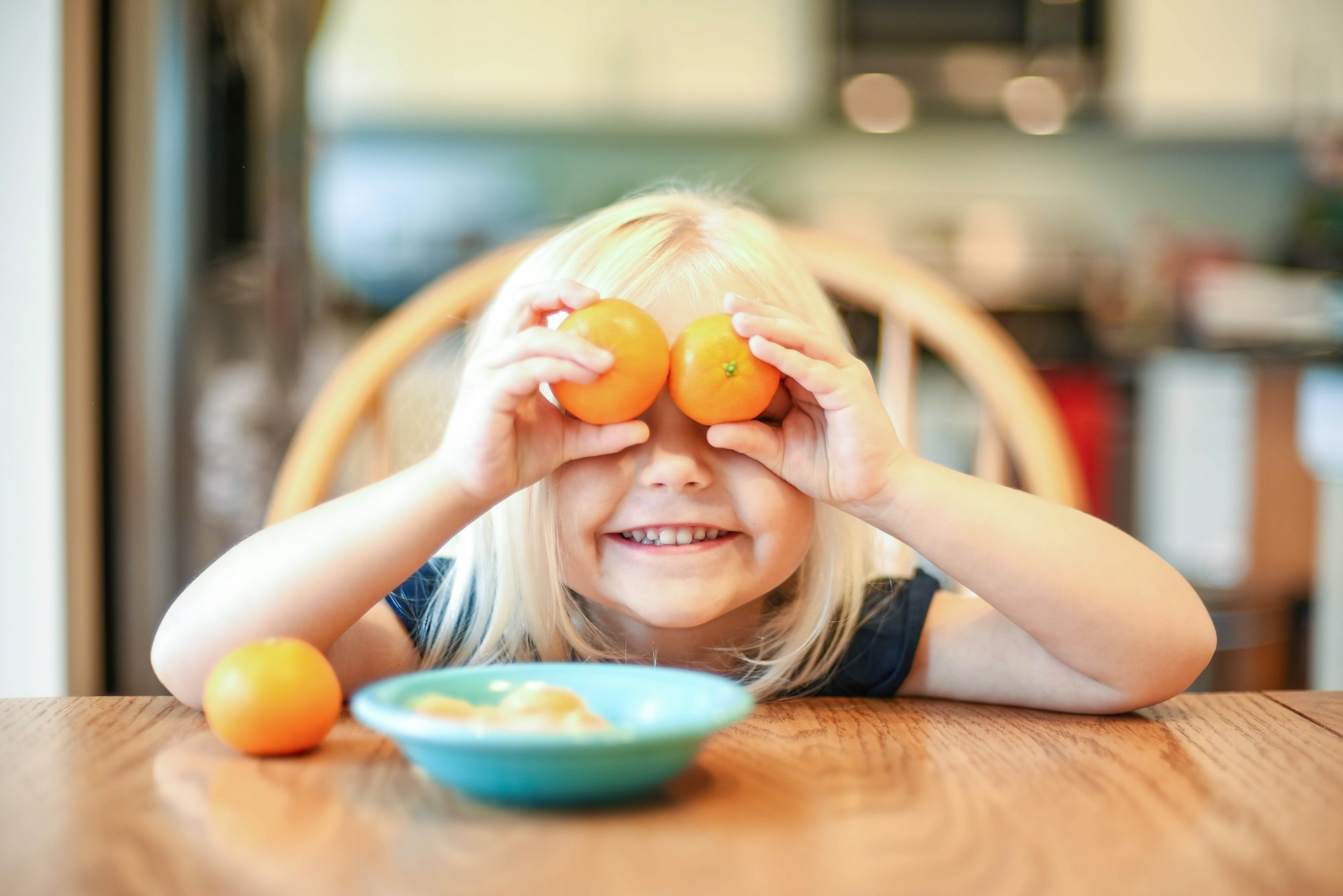 Cute little girl at the kitchen table holding clementines up to her eyes